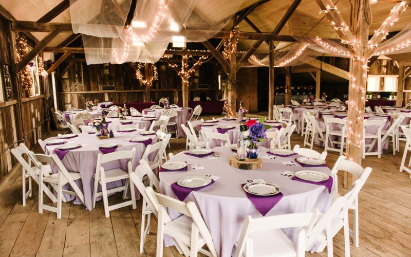 A large room with tables and chairs covered in purple cloth.