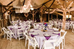 A large room with tables and chairs covered in purple cloth.