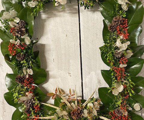 A wreath of leaves and flowers on a white wall.