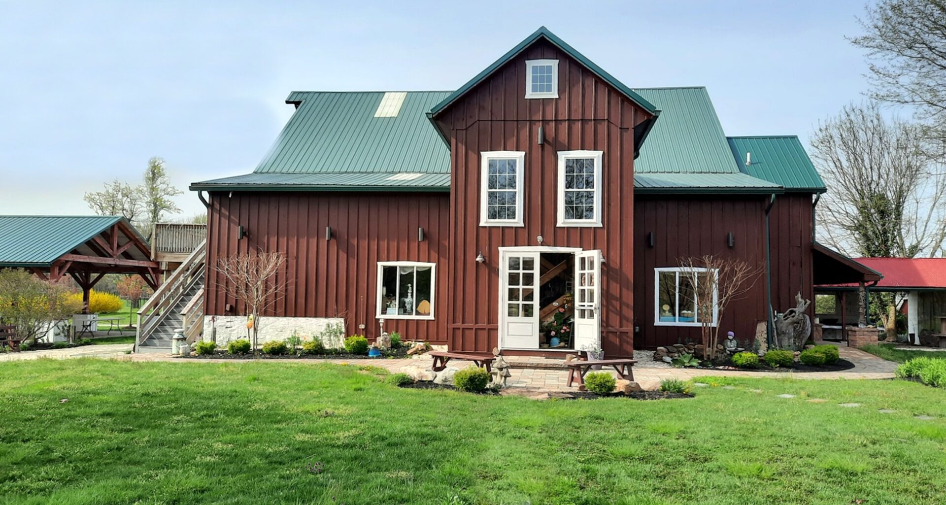 A red barn with green roof and lawn in front of it.