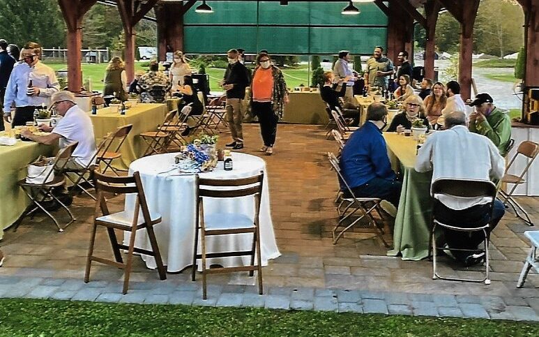 A group of people sitting at tables in an outdoor pavilion.